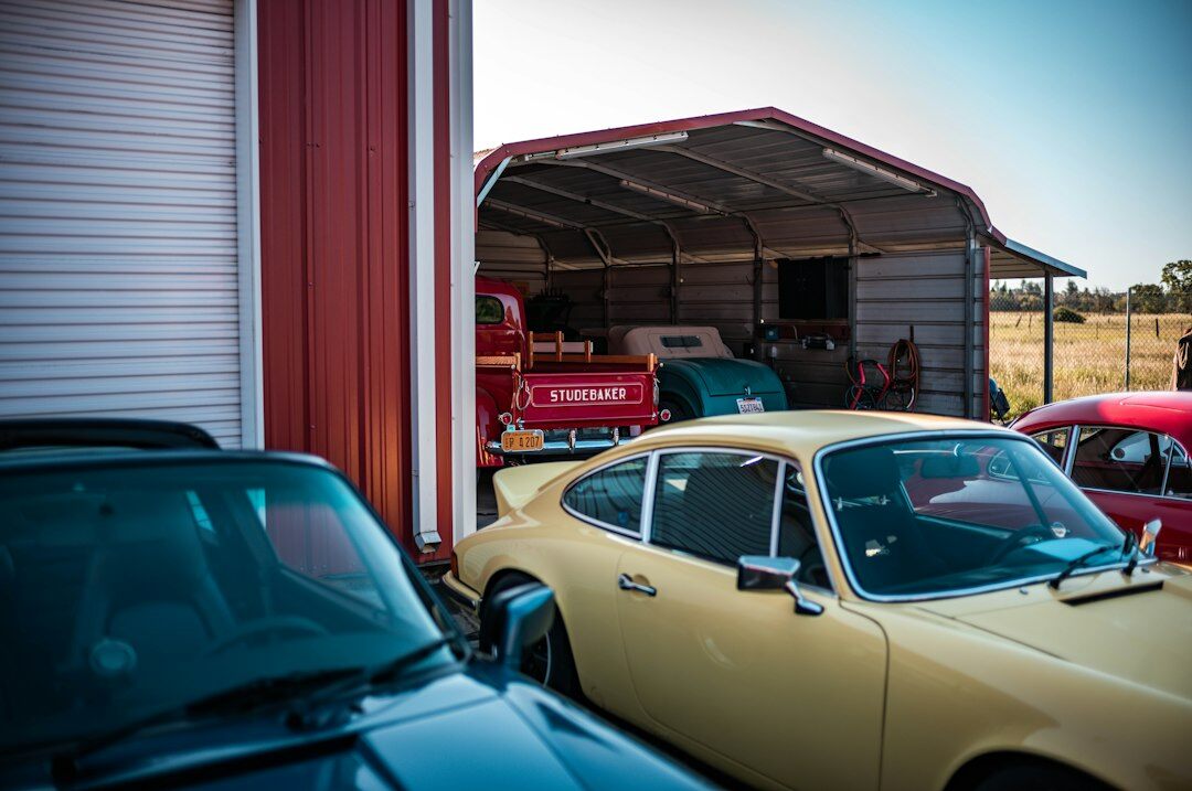 Row of vintage automobiles stored under a corrugated metal roof workshop
